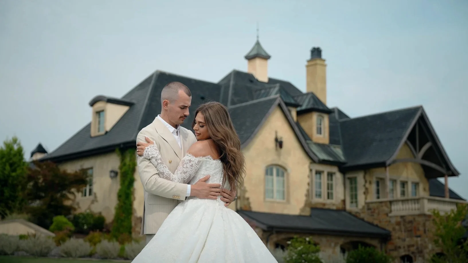 Groom in an ivory suit holding his bride in front of a stone chateau