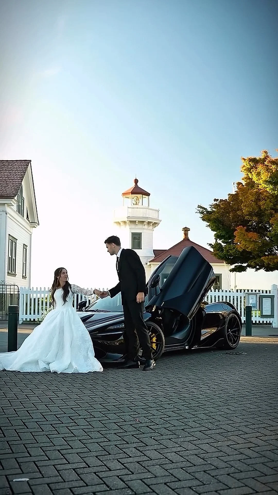 Bride beside a black McLaren with open doors near a lighthouse
