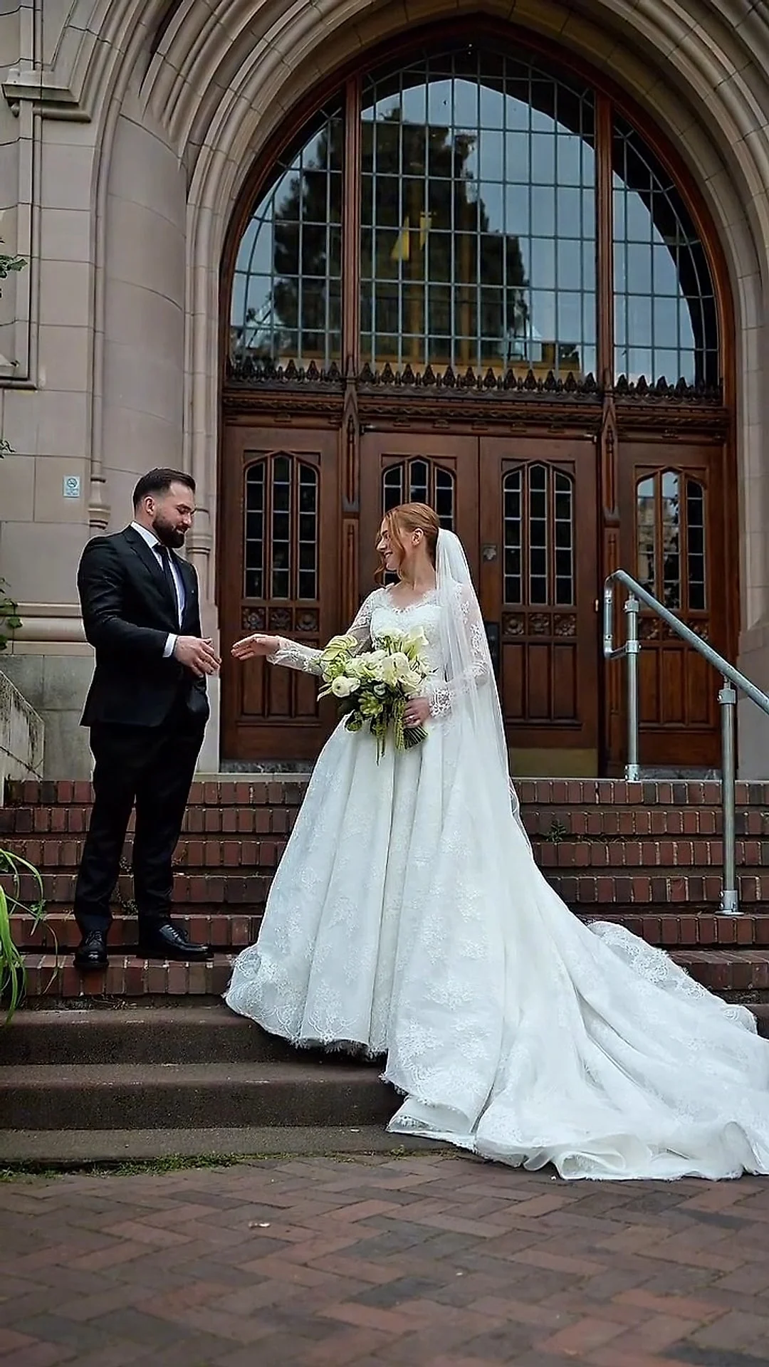 Bride with a long train and the groom on the steps of an arched church entrance