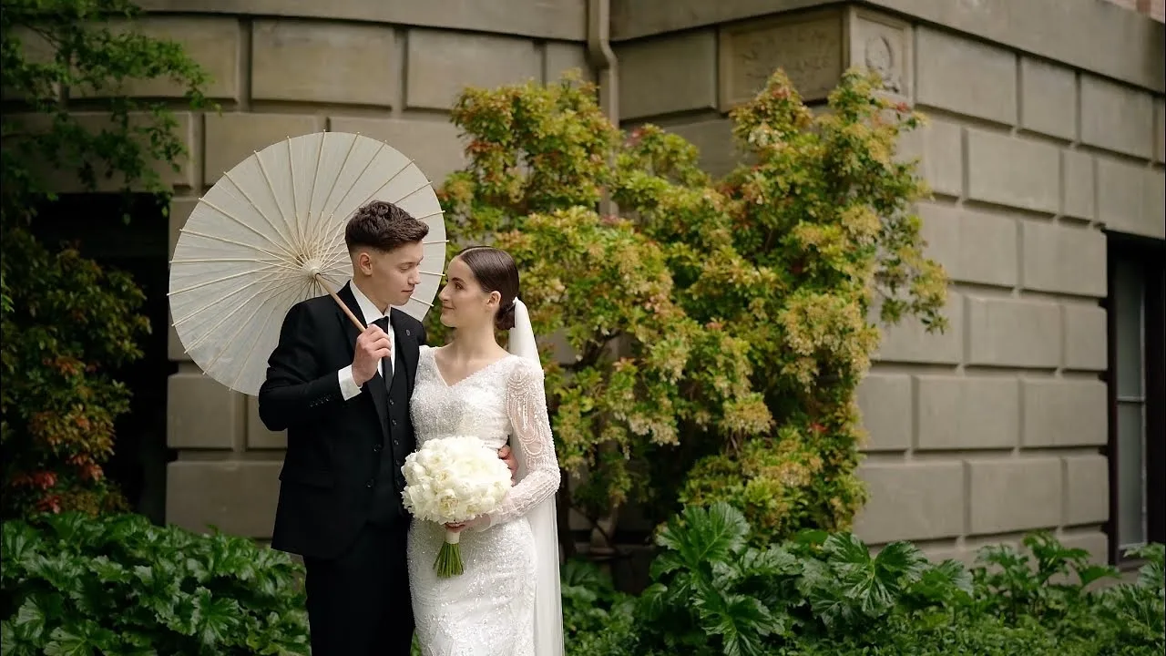 Groom holding a white parasol beside his bride in a garden