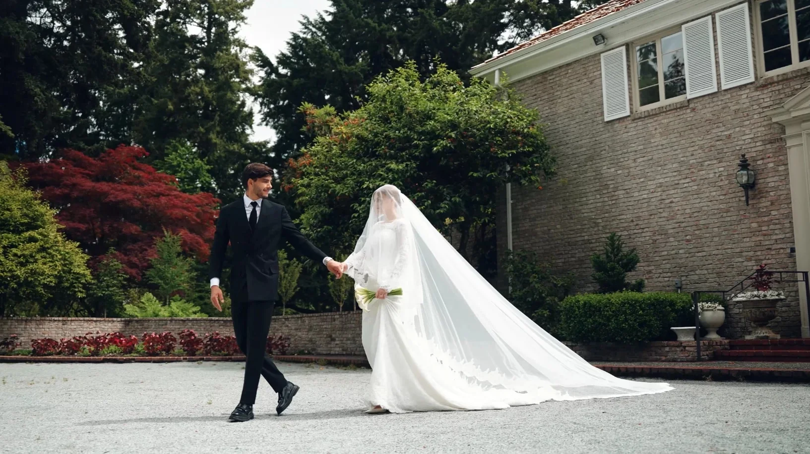 Groom leading his veiled bride by the hand across an estate courtyard